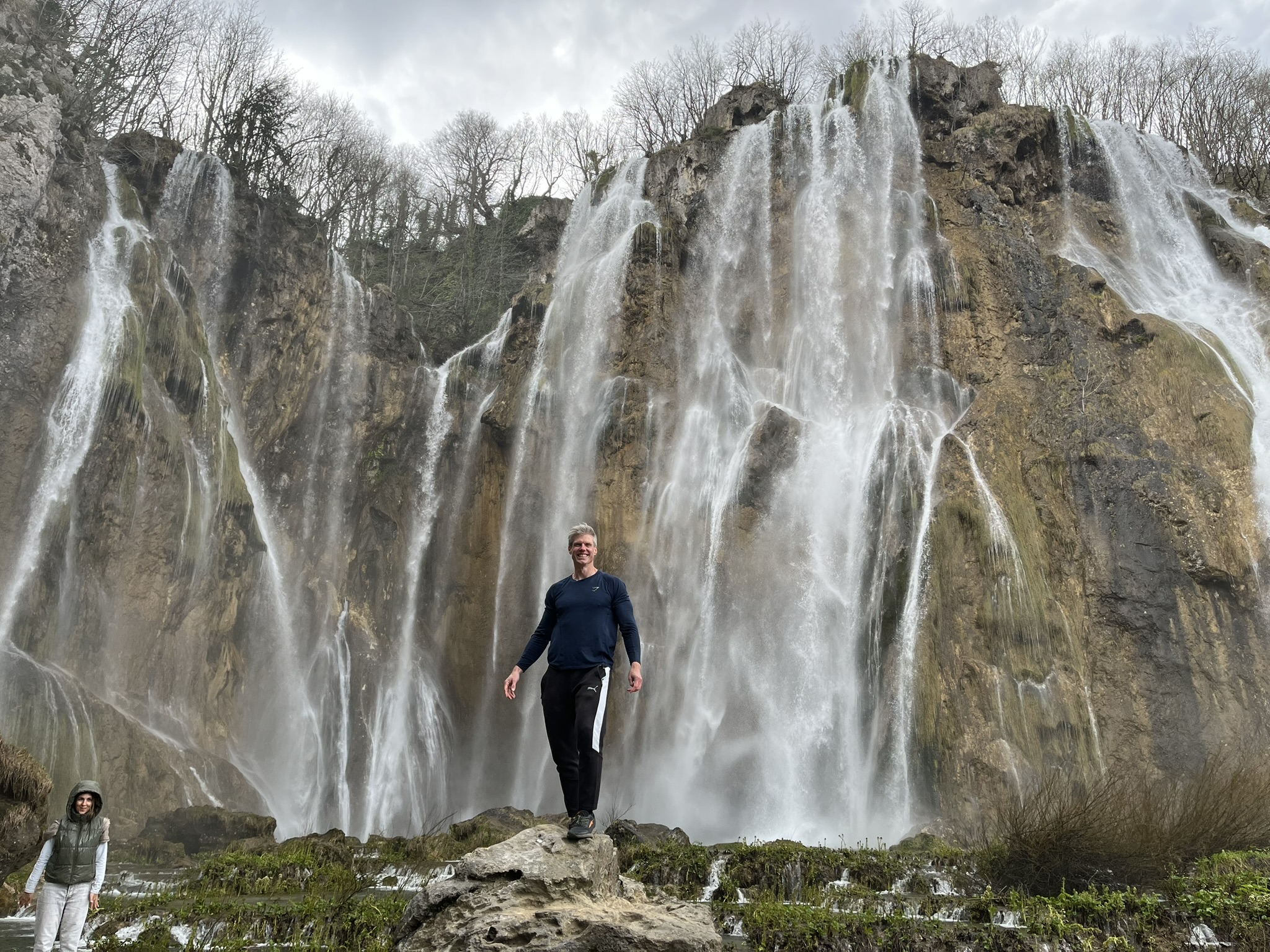 Ben Ogorek smiling in fitness clothes, standing on a rock in front of a waterfall.
